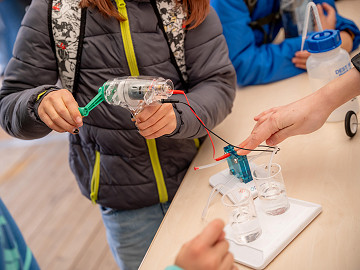 Kinder erzeugen bei mit einem Generator Strom und lernen, wie Energie in einer Brennstoffzelle umgewandelt wird.